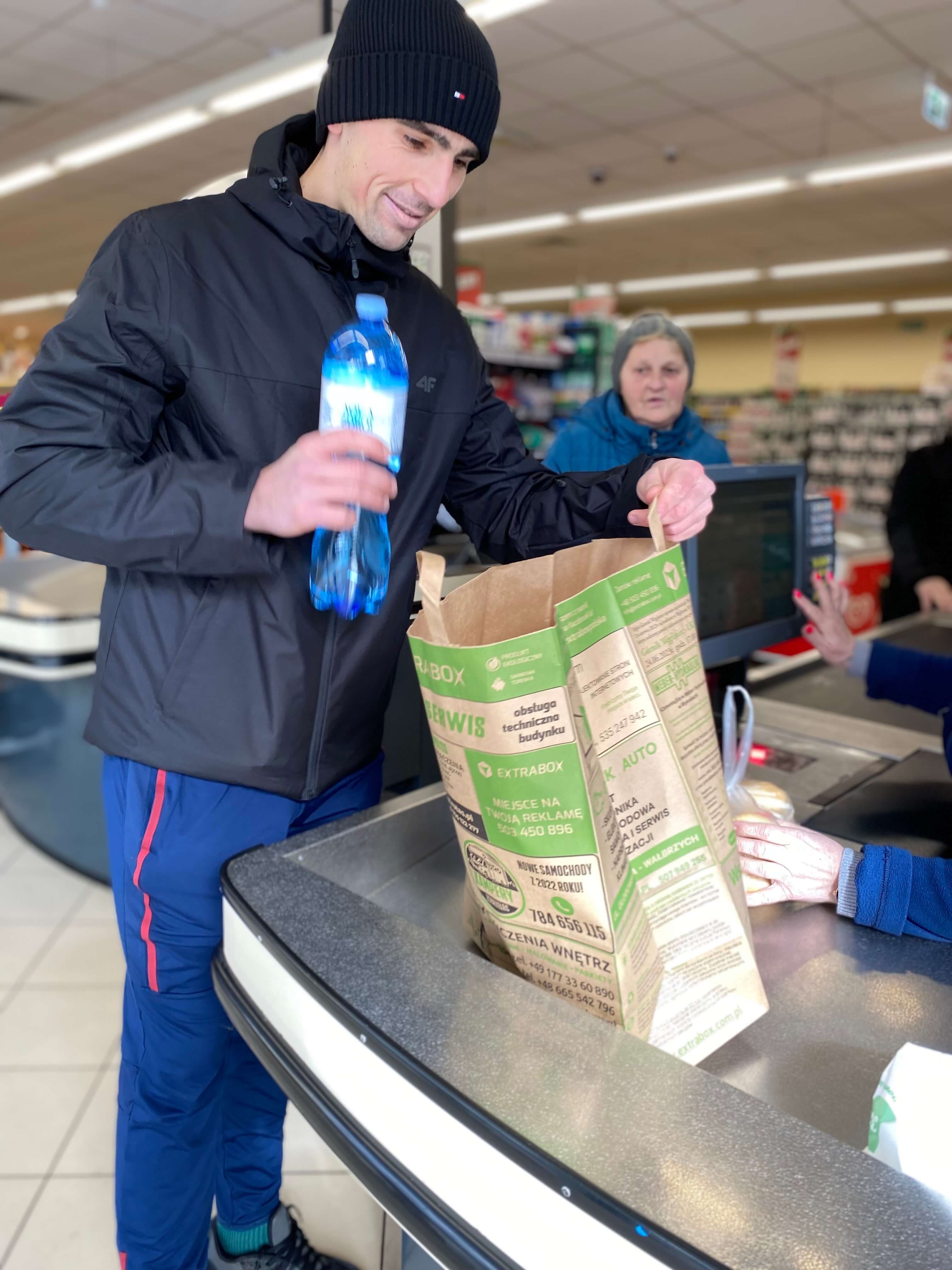 młody mężczyzna pakujący do torby extrabox wodę mineralną